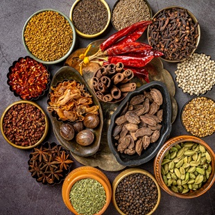 Variety of spices and herbs in bowls against dark backdrop.