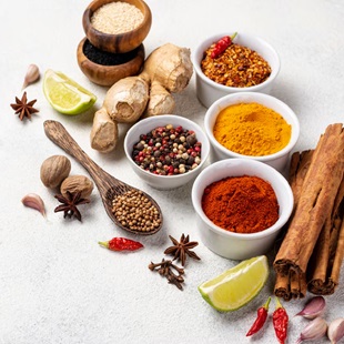 Collection of spices and herbs in bowls on white backdrop.